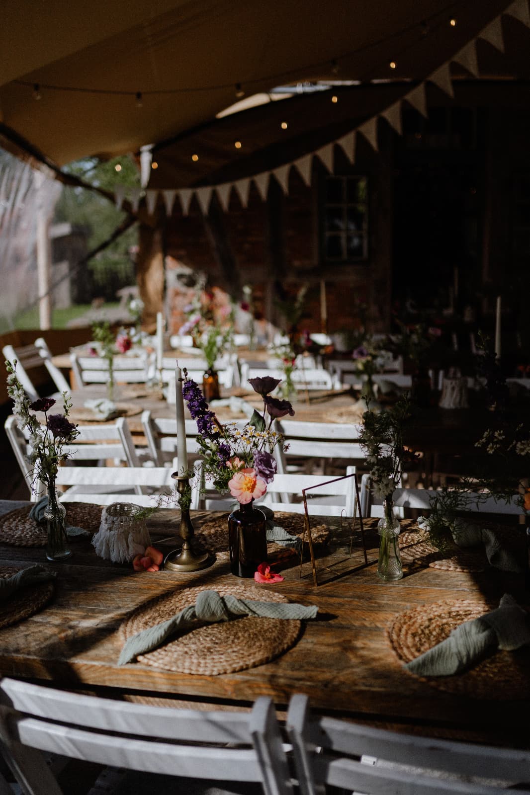 Lange Hochzeitstafel mit Kerzen, Wildblumen und Wimpelketten unter dem Zelt im Abendlicht