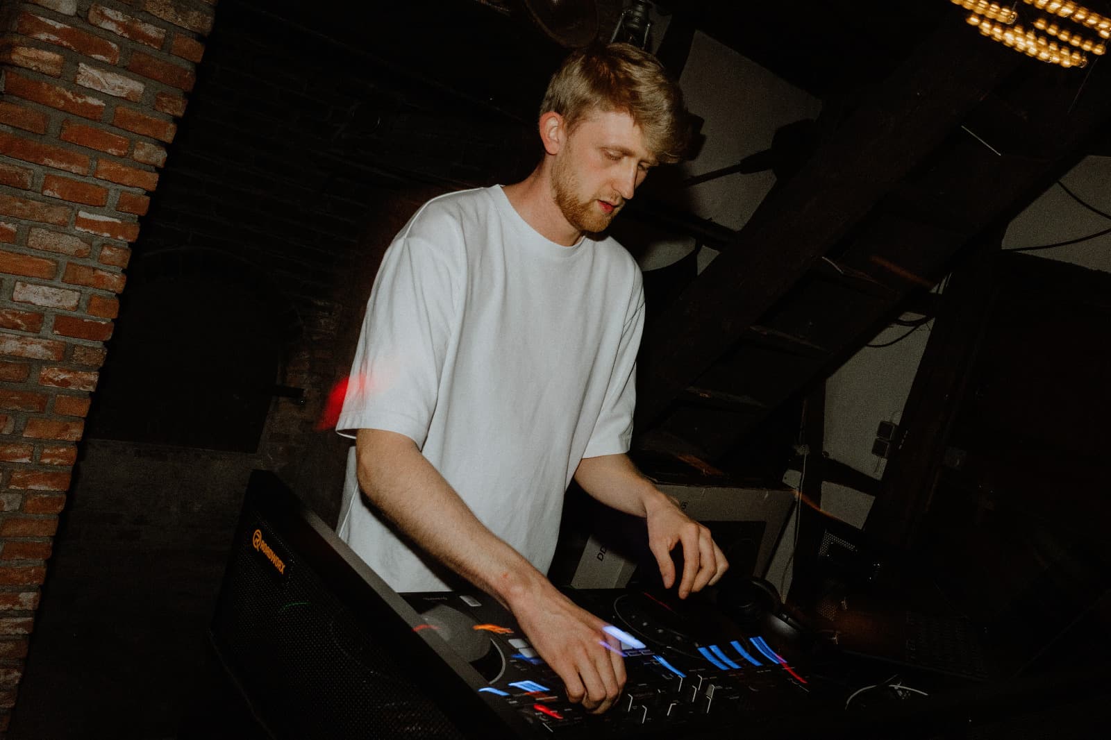 DJ Daku beim Auflegen in der Scheune, hinter ihm Backsteinwand, Holzbalken und warme Lampen