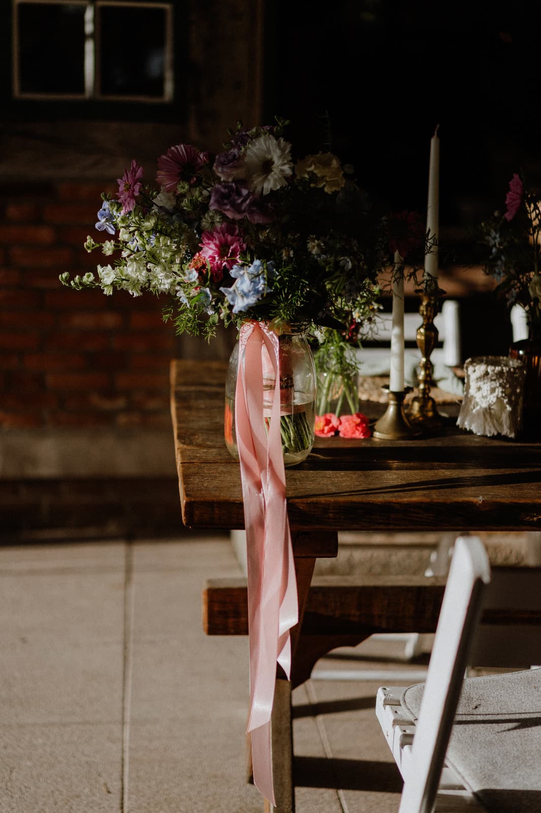 Brautstrauß aus Wildblumen mit rosa Satinbändern auf der Holztafel vor einer Backsteinwand