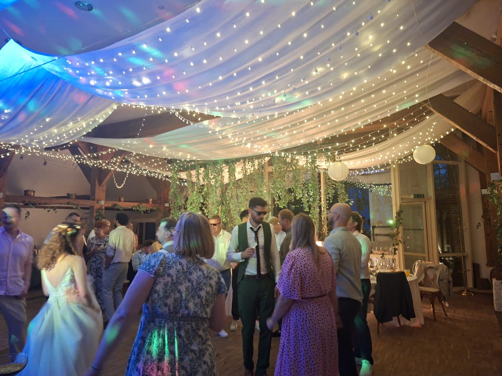 Volle Tanzfläche im Festsaal unter Lichterketten und farbigem Licht während der Hochzeitsparty auf Gut Schöneworth